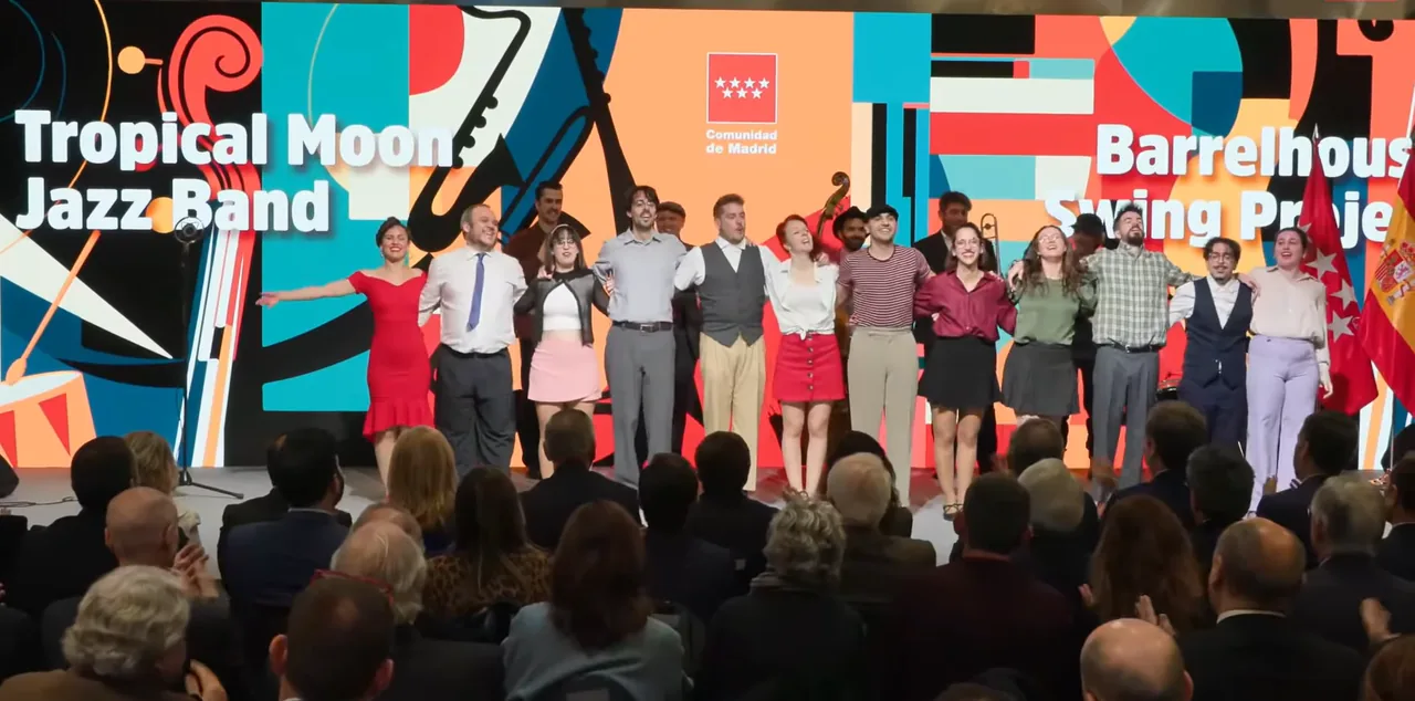 La compañía al completo saludando al público sobre el escenario de la inauguración de FITUR Madrid, con el rótulo de Tropical Moon Jazz Band y Barrelhouse Swing Project al fondo