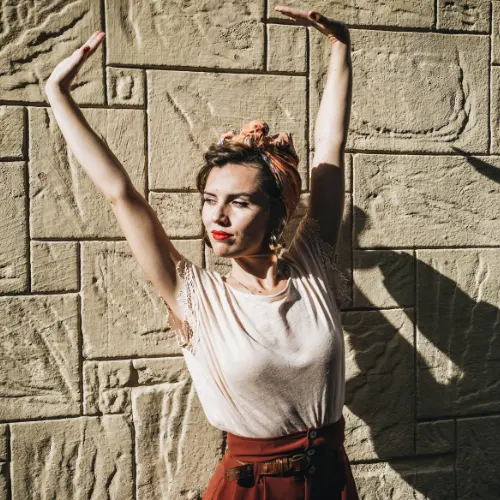 Mujer con los brazos en alto y una flor en el pelo, apoyada en una pared al sol