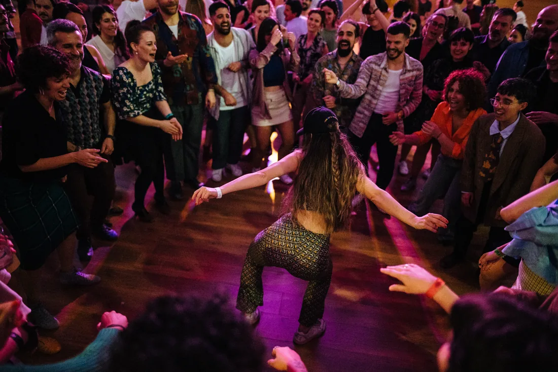 Bailarina en el centro de un corro de gente durante una jam, bajo luz de club