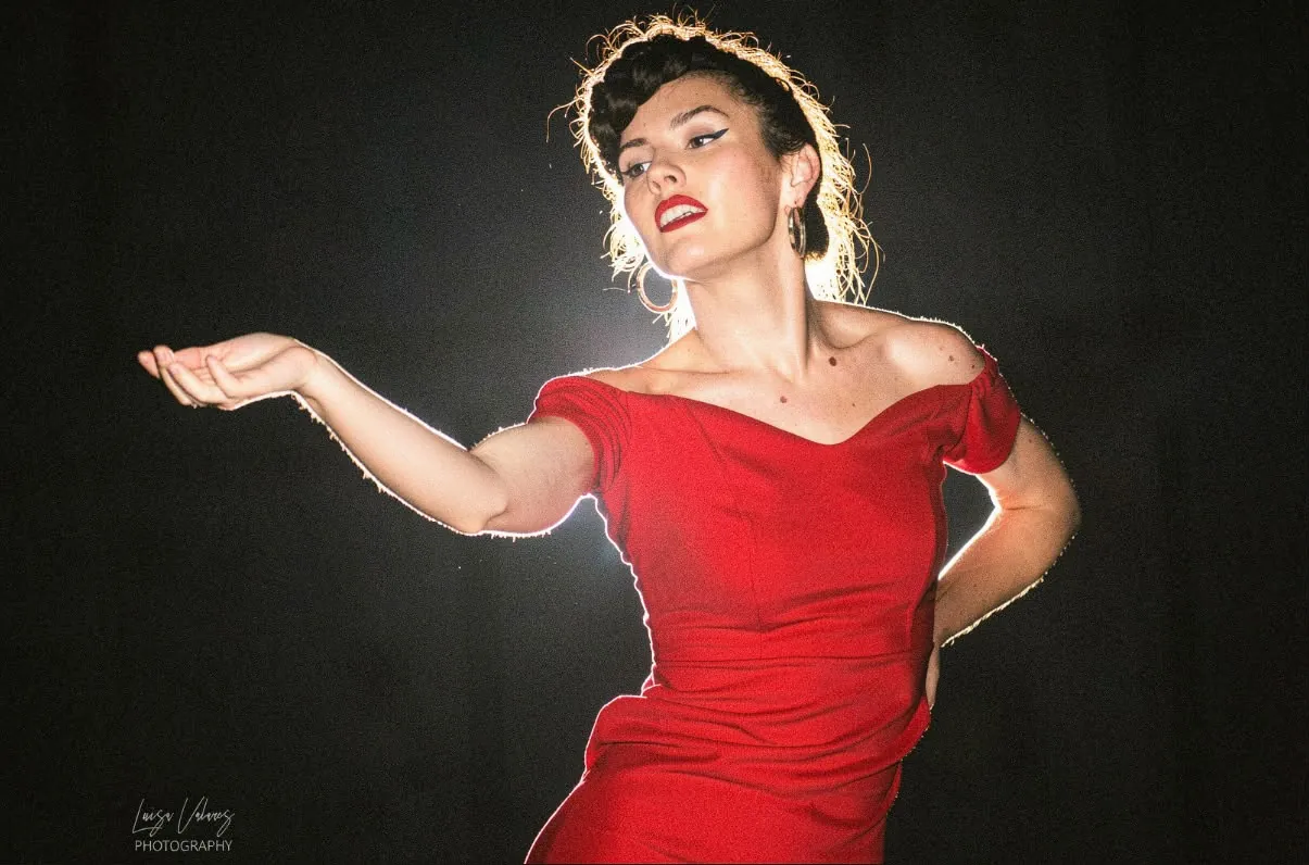 Elisabet Solo con vestido rojo, recortada a contraluz sobre fondo oscuro, con un brazo extendido durante la actuación