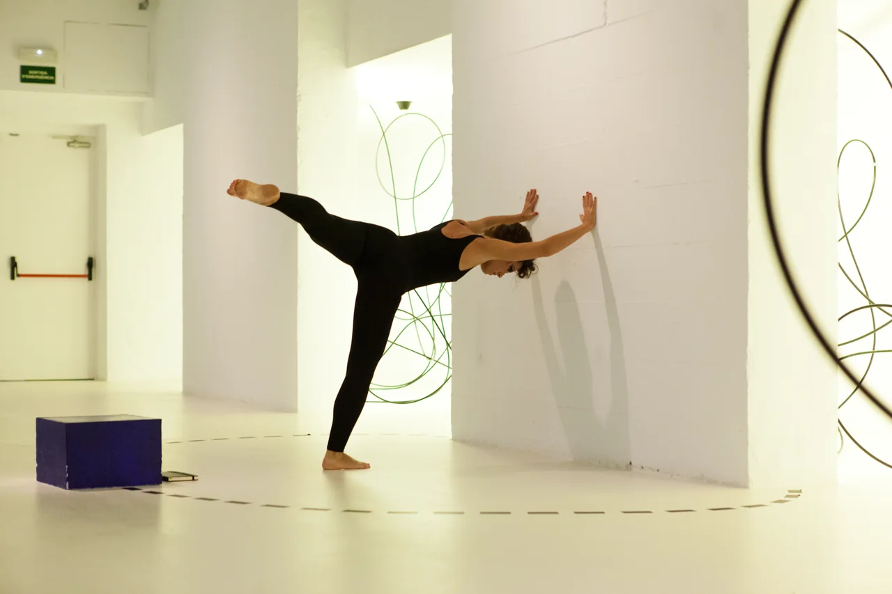 Elisabet Solo en equilibrio apoyada en una pared blanca de la sala, entre trazos verdes de la instalación