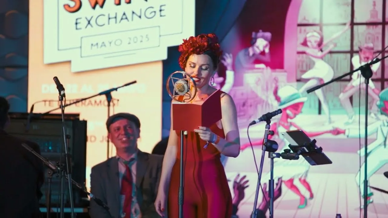 Elisabet Solo, de rojo, ante un micrófono vintage en el Madrid Swing Exchange, con la banda y una proyección de bailarines al fondo
